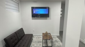 A modern living room with a dark brown sofa, a wooden coffee table, and a fluffy rug. A flat-screen TV is mounted on the wall. - Cozy Corner Rentals (Saskatoon)