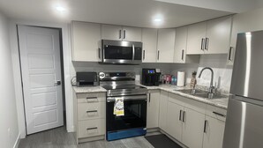 A modern kitchen with stainless steel appliances, white cabinetry, and a wooden floor. - Cozy Corner Rentals (Saskatoon)