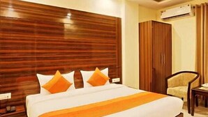 Une chambre d’hôtel avec un grand lit, une tête de lit en bois, un climatiseur et un ventilateur de plafond.