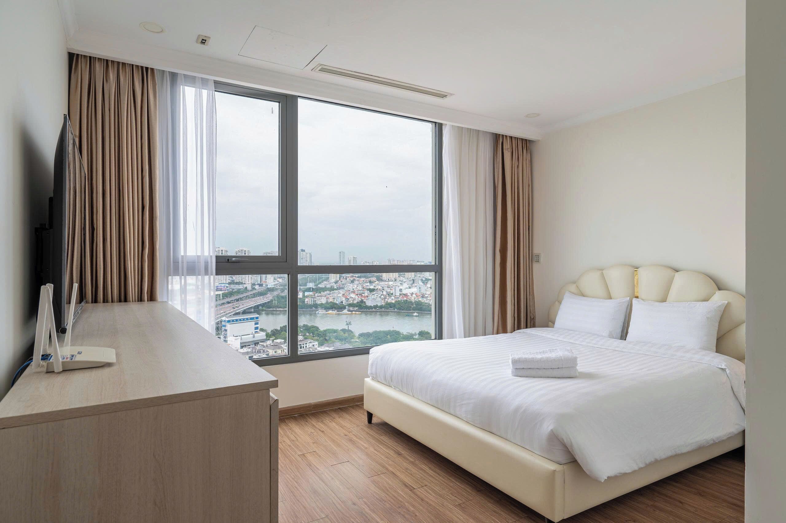 A hotel room with a large window, a bed, a desk, and a television.