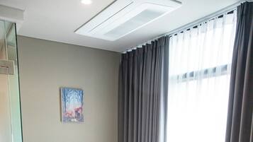 A hotel room with a large bed, a bedside table with a lamp, a painting on the wall, and a window with curtains.