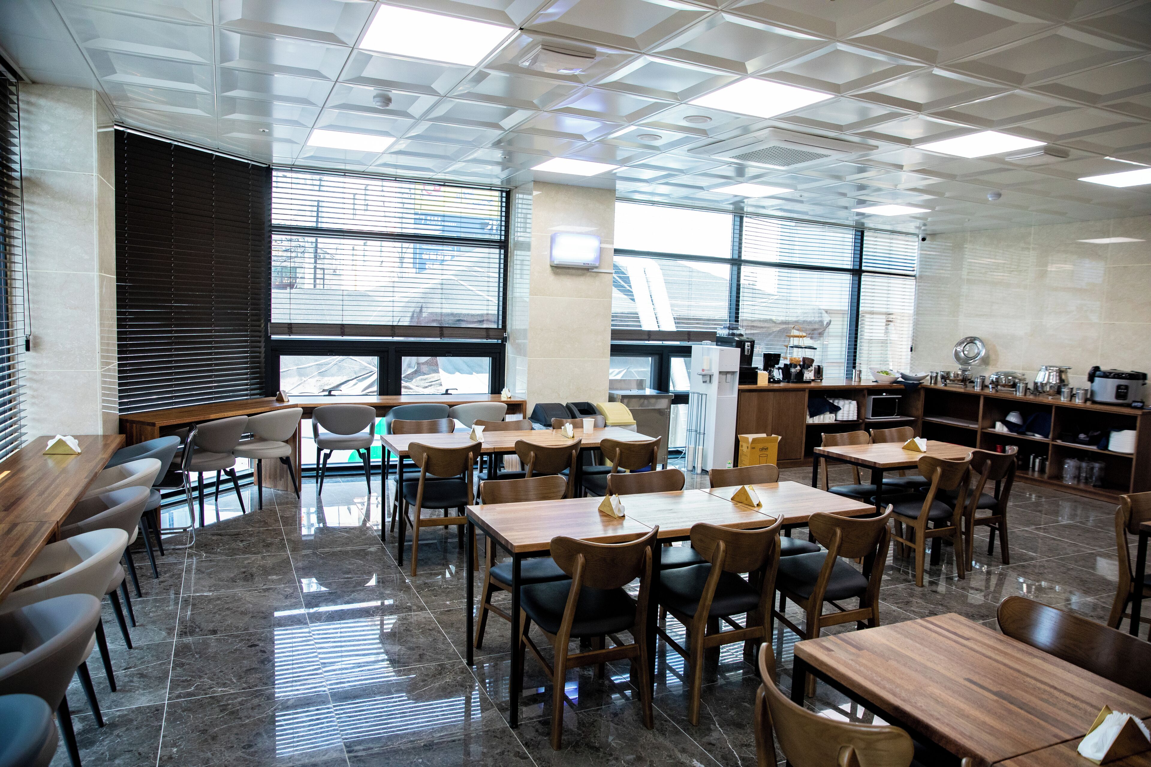 Un espace de restauration moderne, doté de nombreuses tables et chaises, de grandes fenêtres et d’un plafond haut orné d’un motif géométrique.