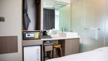 Habitación de hotel con cama, escritorio con microondas, refrigerador pequeño, lavabo y cabina de ducha de vidrio.