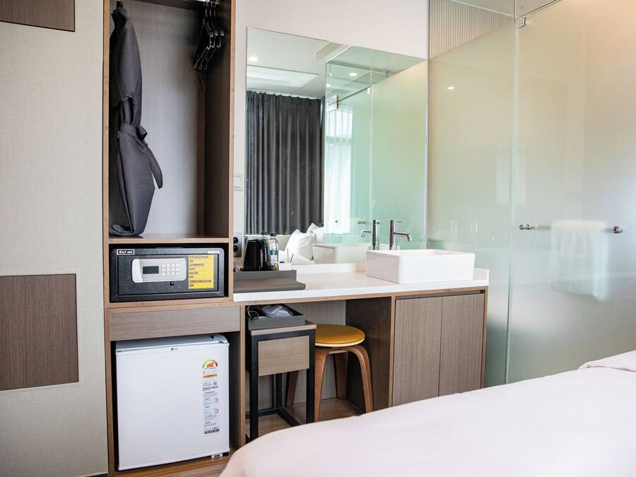 Habitación de hotel con cama, escritorio con microondas, refrigerador pequeño, lavabo y cabina de ducha de vidrio.