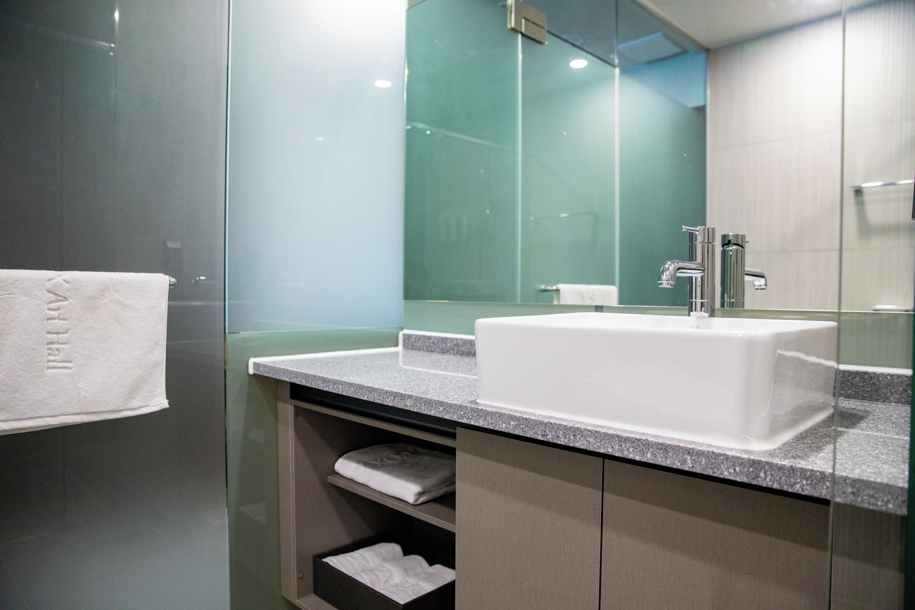 Un baño moderno con lavamanos blanco, cabina de ducha de vidrio y un espejo.