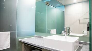 Un baño moderno con cabina de ducha de vidrio, un lavabo blanco y un espejo grande.