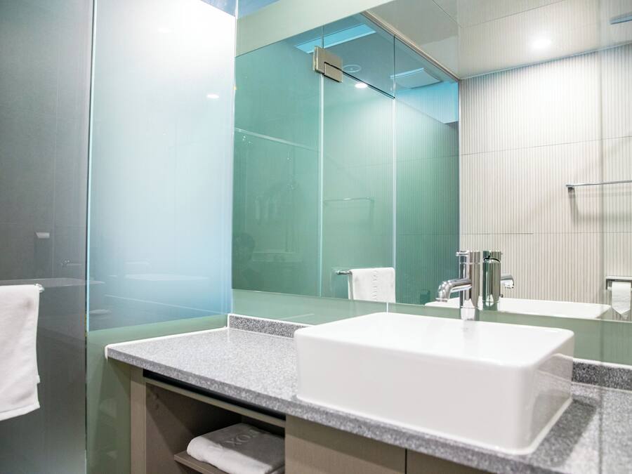 Un baño moderno con cabina de ducha de vidrio, un lavabo blanco y un espejo grande.