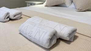 Een net opgemaakt bed met witte lakens en een hoofdbord, een nachtkastje met een lamp, en een stopcontact aan de muur.