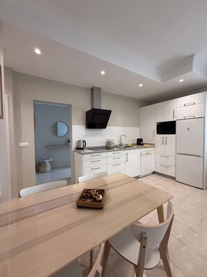 Una cocina moderna con armarios blancos, un microondas negro y un hervidor de acero inoxidable.