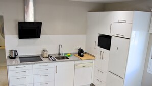 Een keuken met witte kasten, een roestvrijstalen spoelbak, een magnetron en een koelkast.