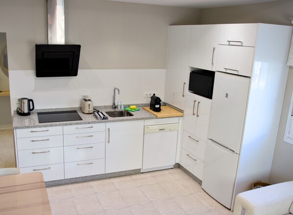 Una cocina con armarios blancos, un lavamanos de acero inoxidable, un microondas y un refrigerador.