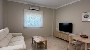 Een moderne woonkamer met een bank, een salontafel, een televisie en een eettafel met stoelen.