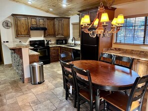 A kitchen with wooden cabinets, a granite countertop, a black stove, a sink, a refrigerator, and a chandelier.