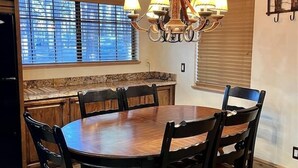 Une salle à manger avec une table et des chaises en bois, un lustre et une fenêtre avec des stores.