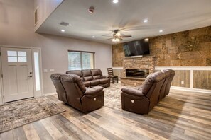 A living room with a fireplace, leather recliners, a ceiling fan, and a TV.