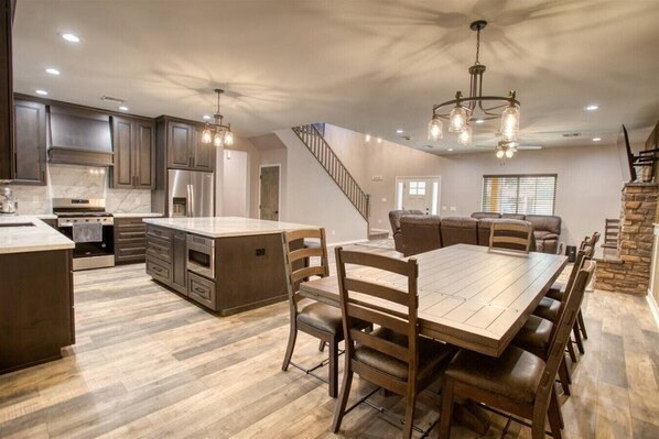 A spacious kitchen with a central island, a dining area with a wooden table and chairs, and a staircase leading to another level.