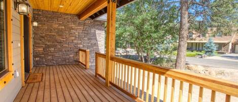 Une terrasse en bois avec des murs en pierre, une balustrade et une vue sur des arbres et un bâtiment au loin.