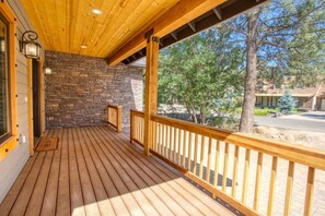 A wooden deck with stone walls, a railing, and a view of trees and a building in the background.