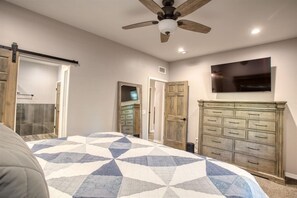 A bedroom with a bed, a ceiling fan, a dresser, and a TV mounted on the wall.