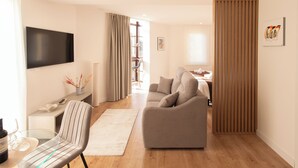 A modern living room with a sofa, a TV mounted on the wall, a dining table with chairs, and a wooden floor.