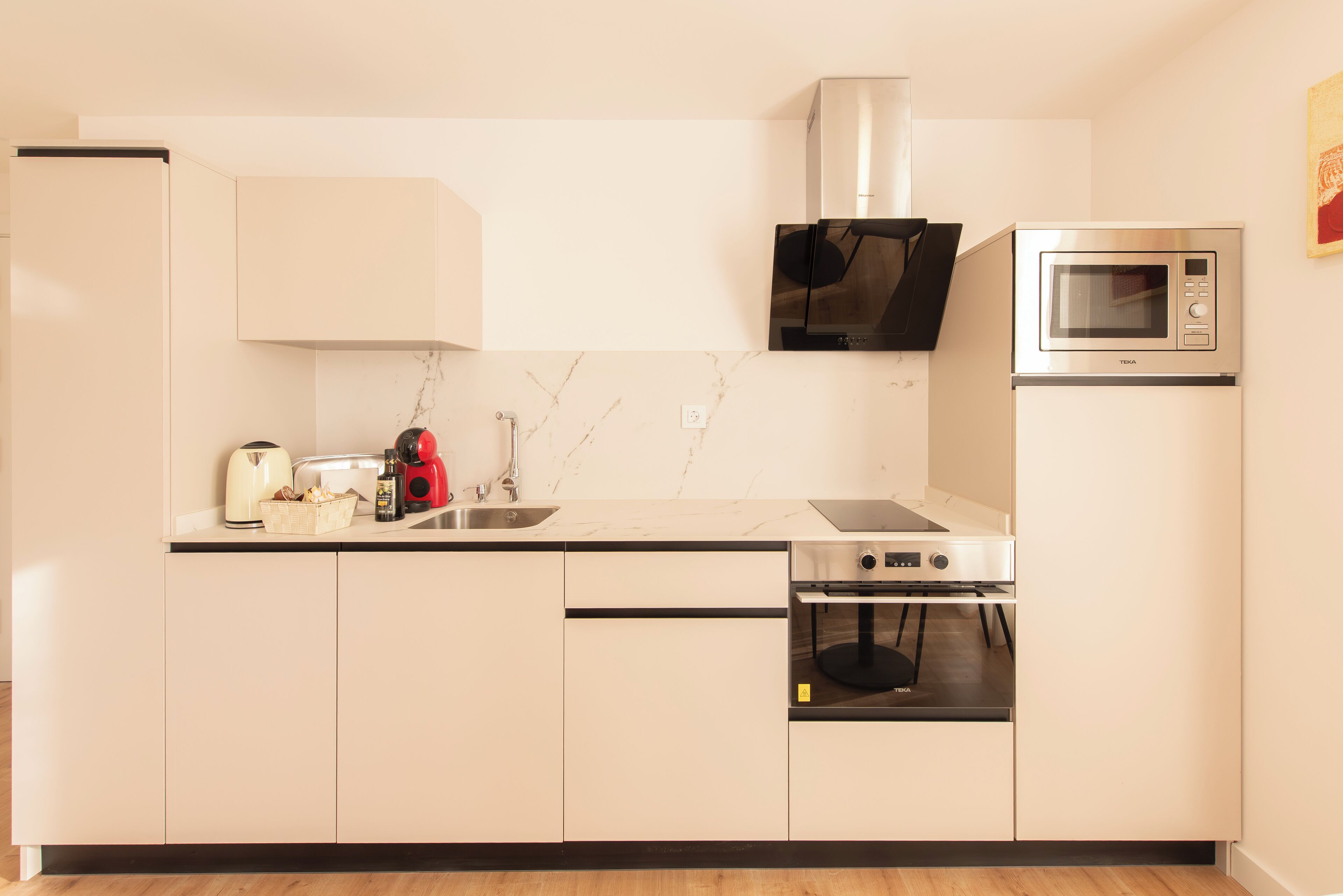 Una cocina moderna con gabinetes blancos, un microondas de acero inoxidable, un horno empotrado y una cafetera.