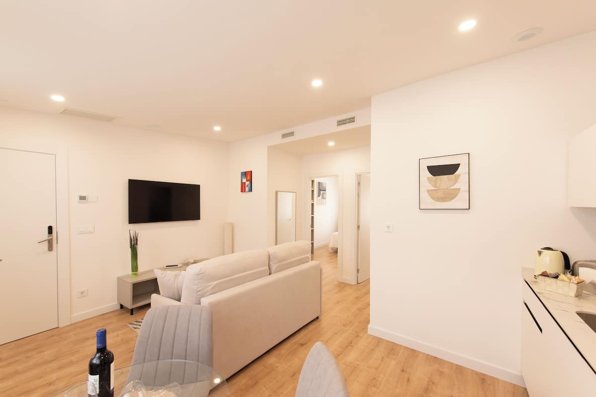 A modern living room with a sofa, a flat-screen TV, and a dining area with a kitchen counter.