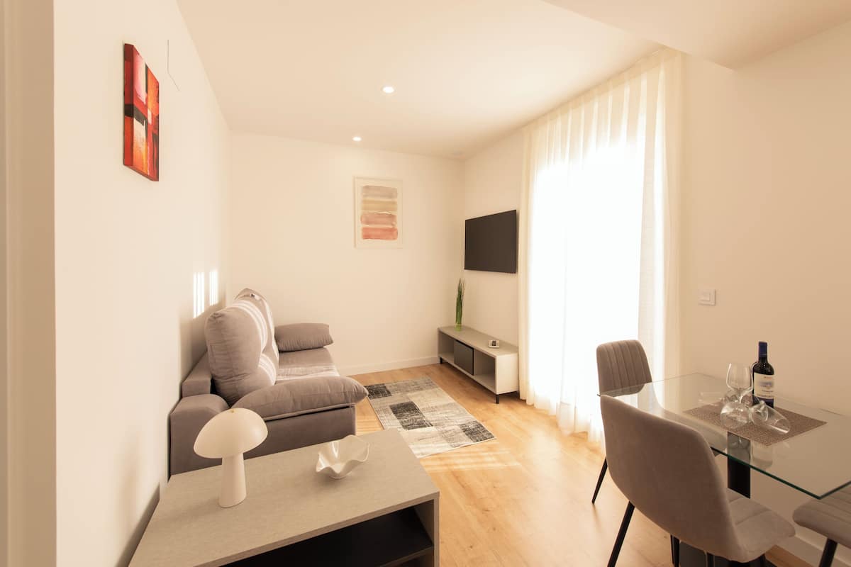 A modern living room with a sofa, a glass table, and a TV mounted on the wall.