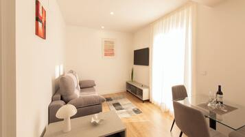 A modern living room with a sofa, a glass table, and a TV mounted on the wall.