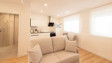 A modern apartment with a living area featuring a beige sofa, a kitchen with a microwave, and a glass shower enclosure.