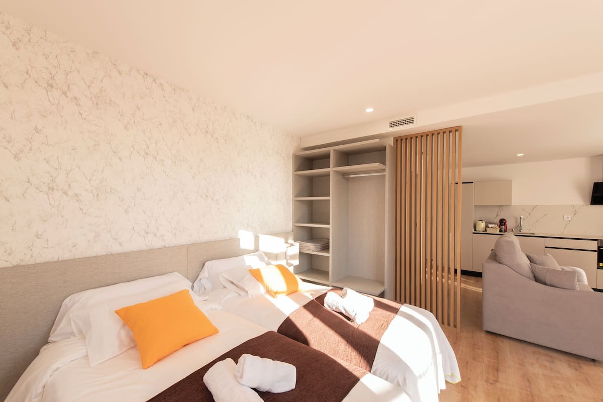 A hotel room with two beds, a sofa, a wardrobe, and a kitchen area.