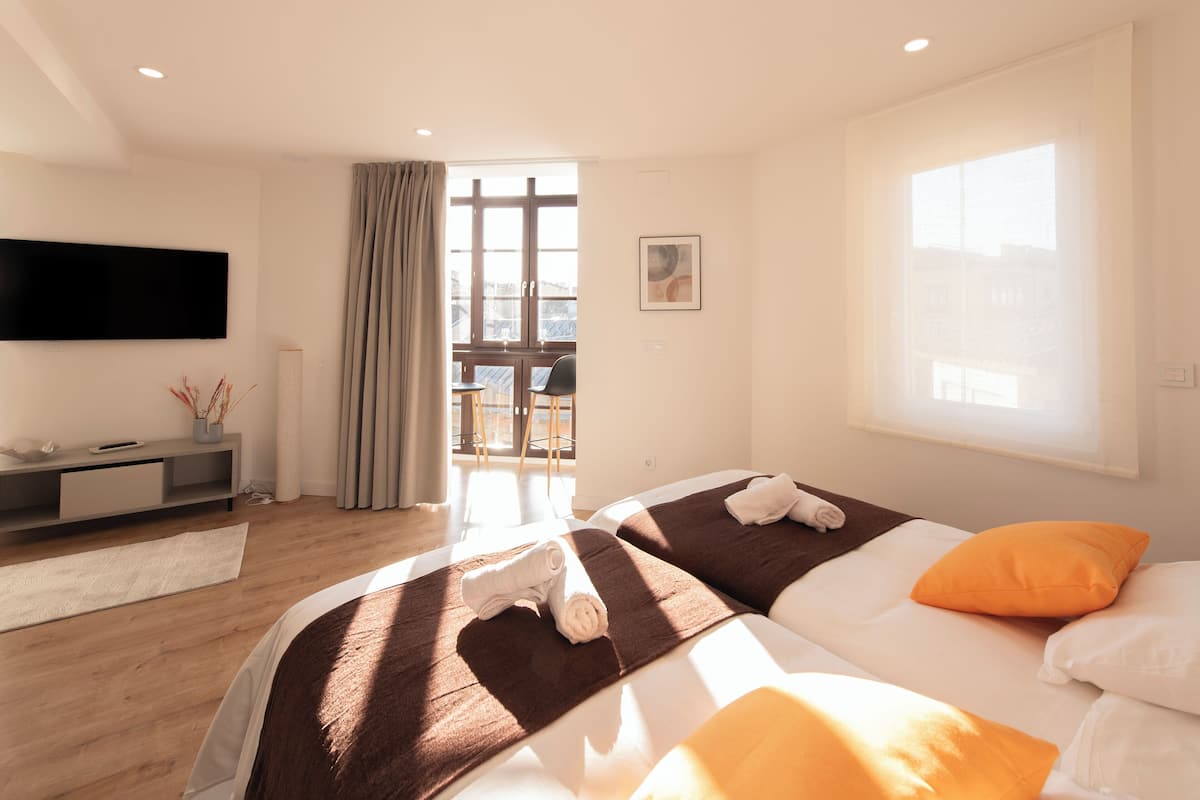 A hotel room with two beds, a flat-screen TV, a balcony, and a view of the city.