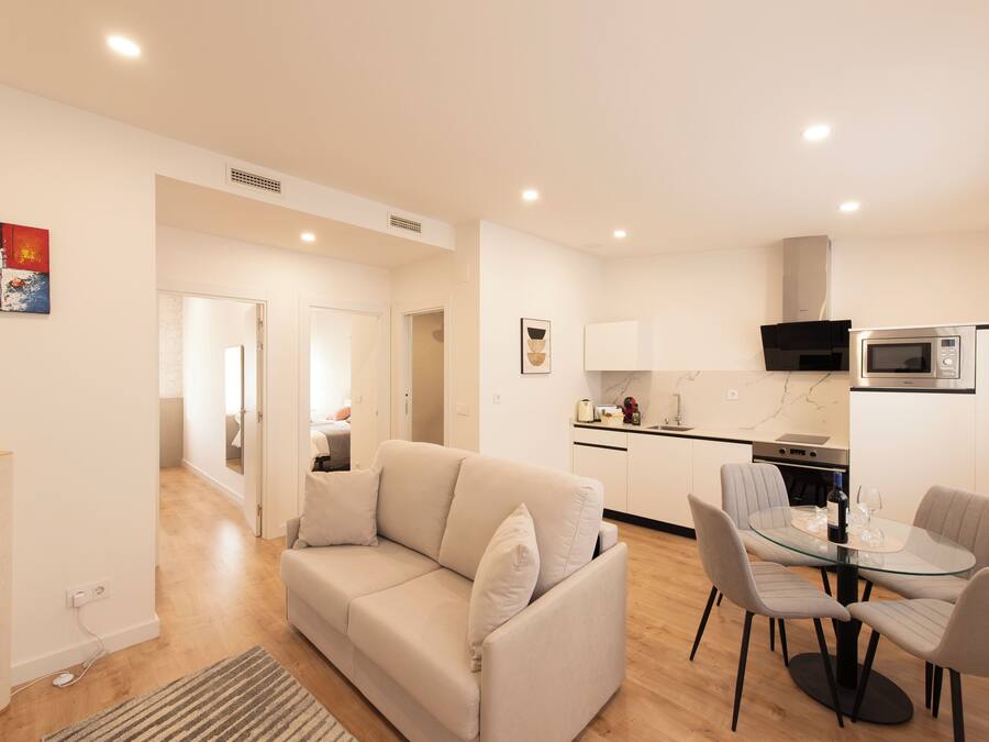 Una sala de estar moderna con un sofá color beige, una mesa de comedor de vidrio y una cocina equipada con microondas y estufa.
