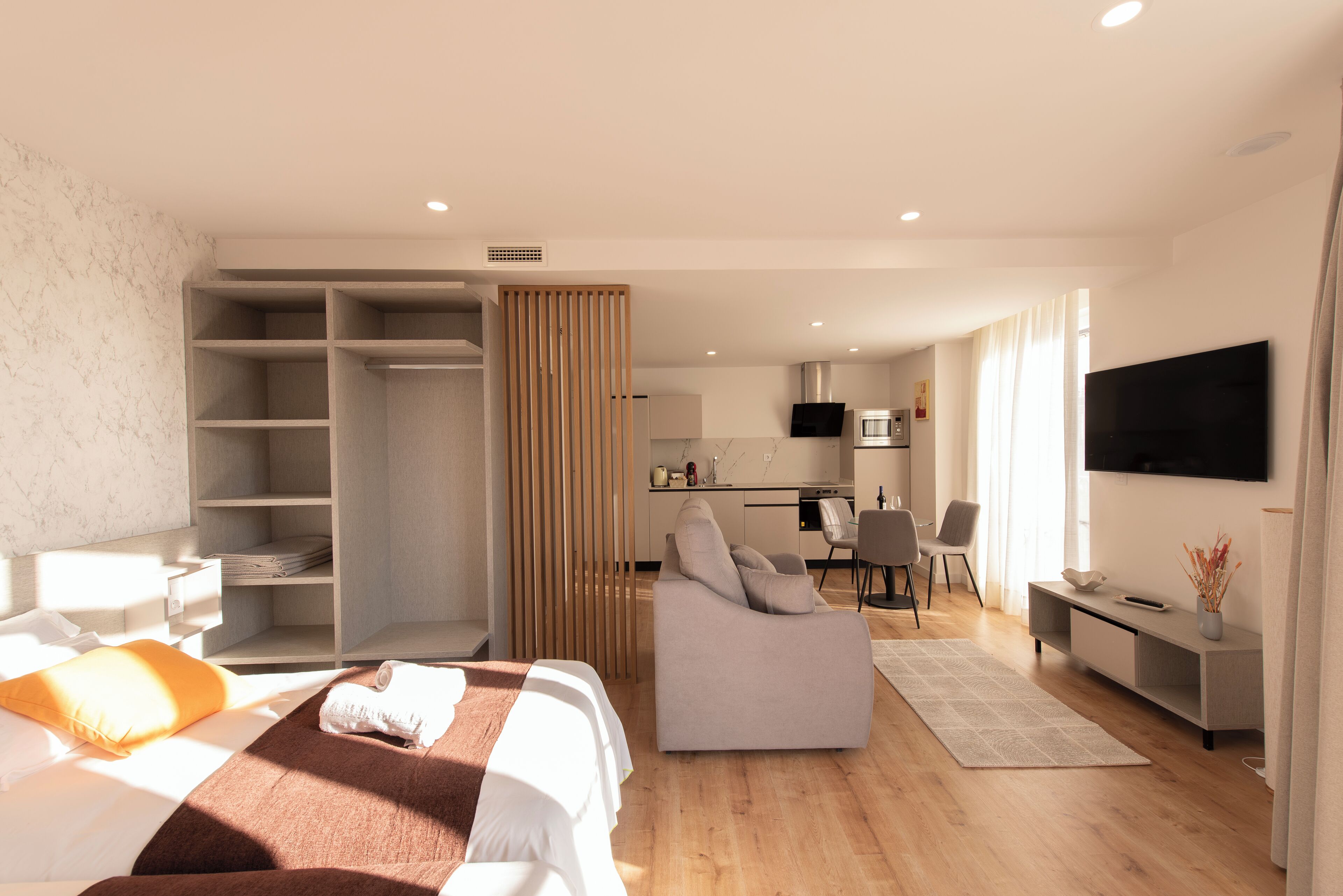 A modern hotel room with a bed, a sofa, a desk, and a TV.