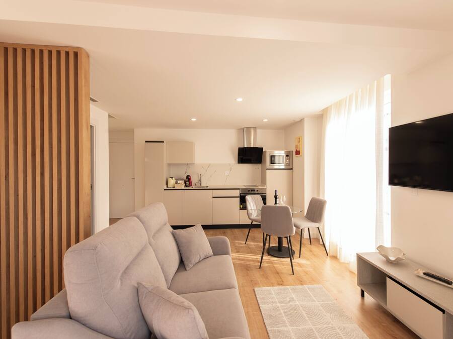 Una sala de estar moderna con un sofá gris, un televisor de pantalla plana y una zona de comedor con sillas y una mesa.