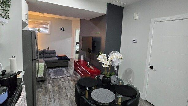 A modern kitchen with a dining area, a living room, and a TV. - Stylish 2BD Basement Suite Close to WEM (Edmonton)