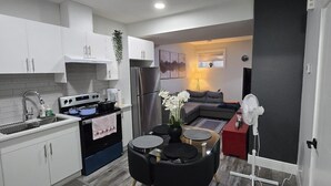 A modern kitchen with white cabinets, a black stove, and a dining area with a black table and chairs. - Stylish 2BD Basement Suite Close to WEM (Edmonton)
