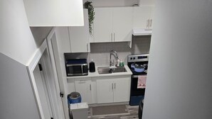 A narrow staircase leading to a kitchen with white cabinets, a microwave, and a sink. - Stylish 2BD Basement Suite Close to WEM (Edmonton)
