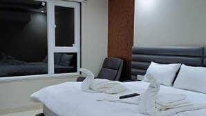 A modern hotel room with a large bed, a window, a chair, and a headboard. - Kiwi Inn Hotel (Ujjain)