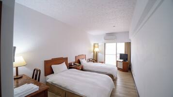 A hotel room with two beds, a desk with a lamp, a chair, a TV, and a window with curtains.