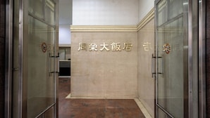 A corridor with glass doors, a tiled floor, and a wall with a sign. - Glory hotel (Luodong)