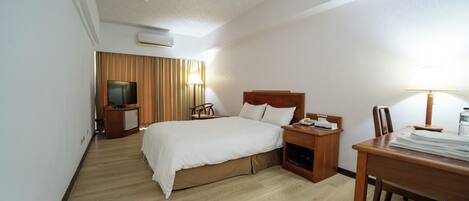 Una habitación de hotel con cama, mesita de noche, lámpara, televisor y escritorio con silla.