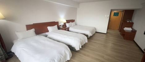 A hotel room with two single beds, a wooden headboard, a bedside table with a lamp, and a wooden floor.