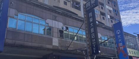 A multi-story hotel with balconies, large windows, and signage for the same hotel and a nearby business.