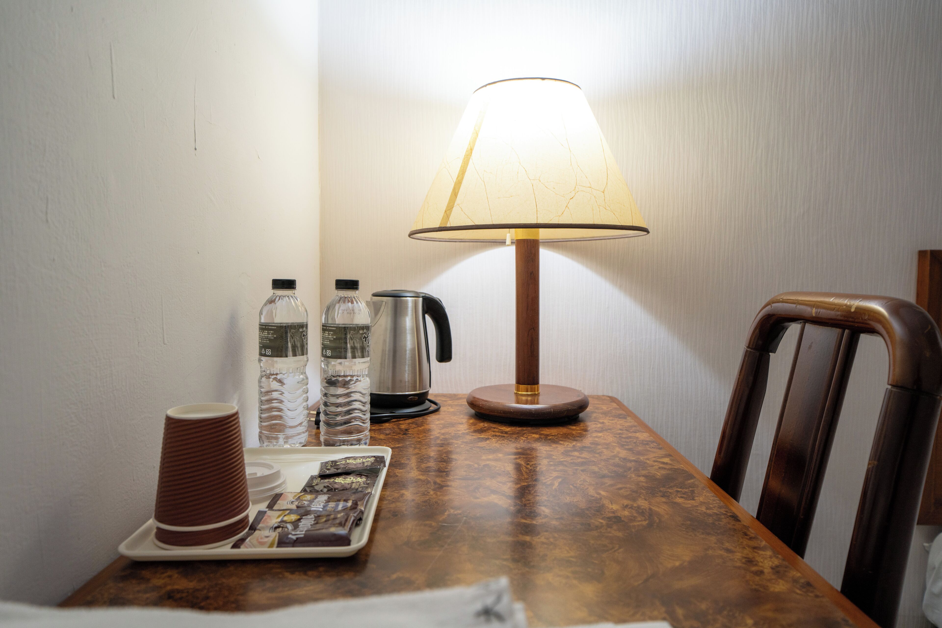 A wooden table with a lamp, a kettle, water bottles, and a tray with a newspaper.