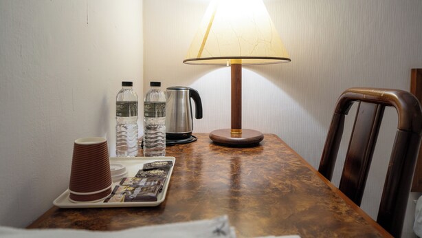 A wooden table with a lamp, a kettle, water bottles, and a tray with a newspaper. - Glory hotel (Luodong)