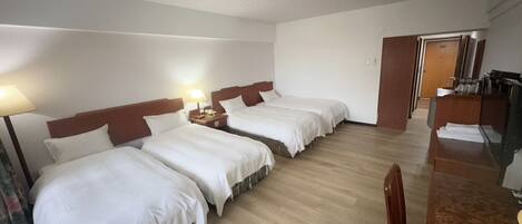 Ein Hotelzimmer mit drei Einzelbetten, einem Holztisch und einem Stuhl.