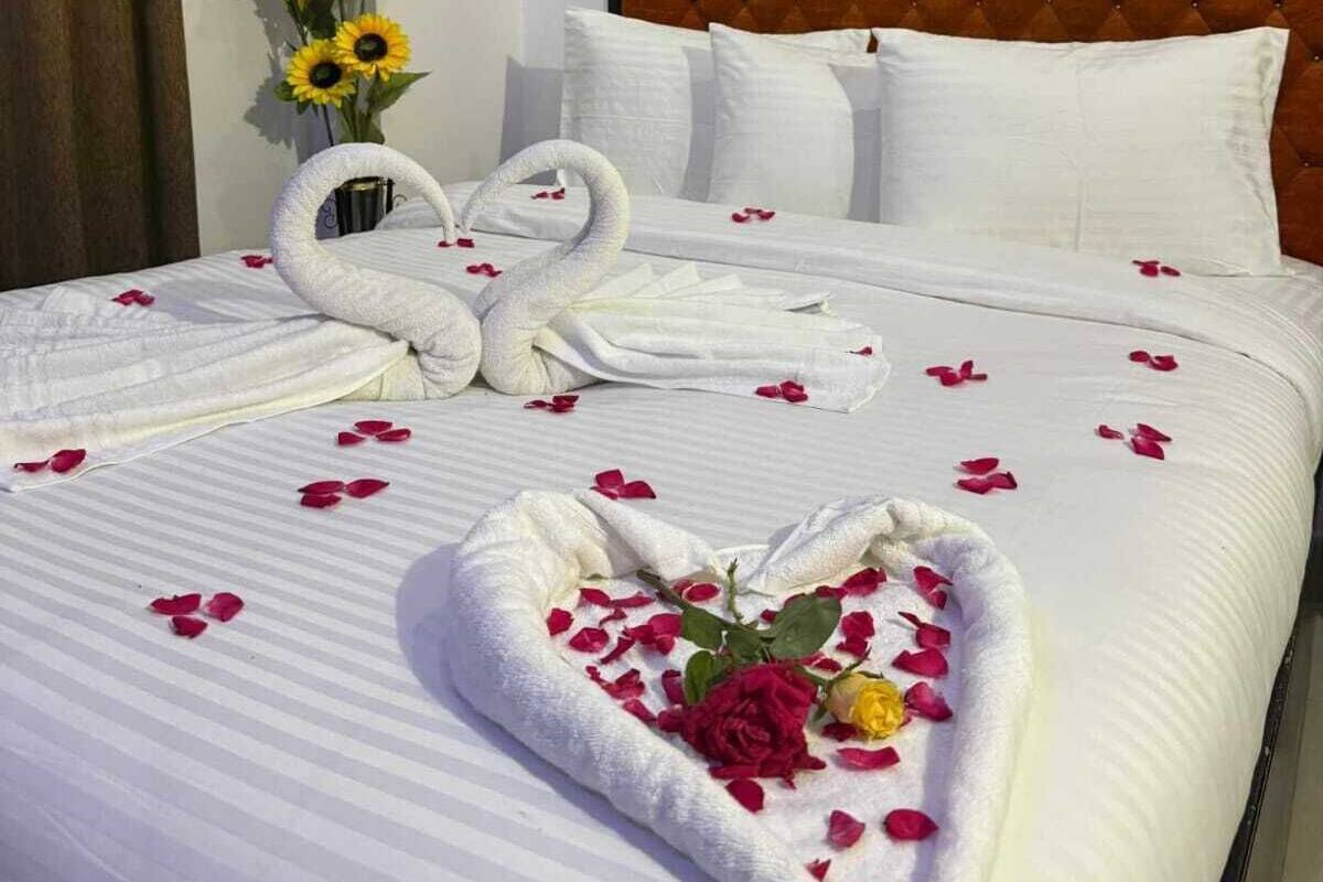 Habitación de hotel con una cama grande, ropa de cama blanca, un cabecero capitonado y un ramo de girasoles.