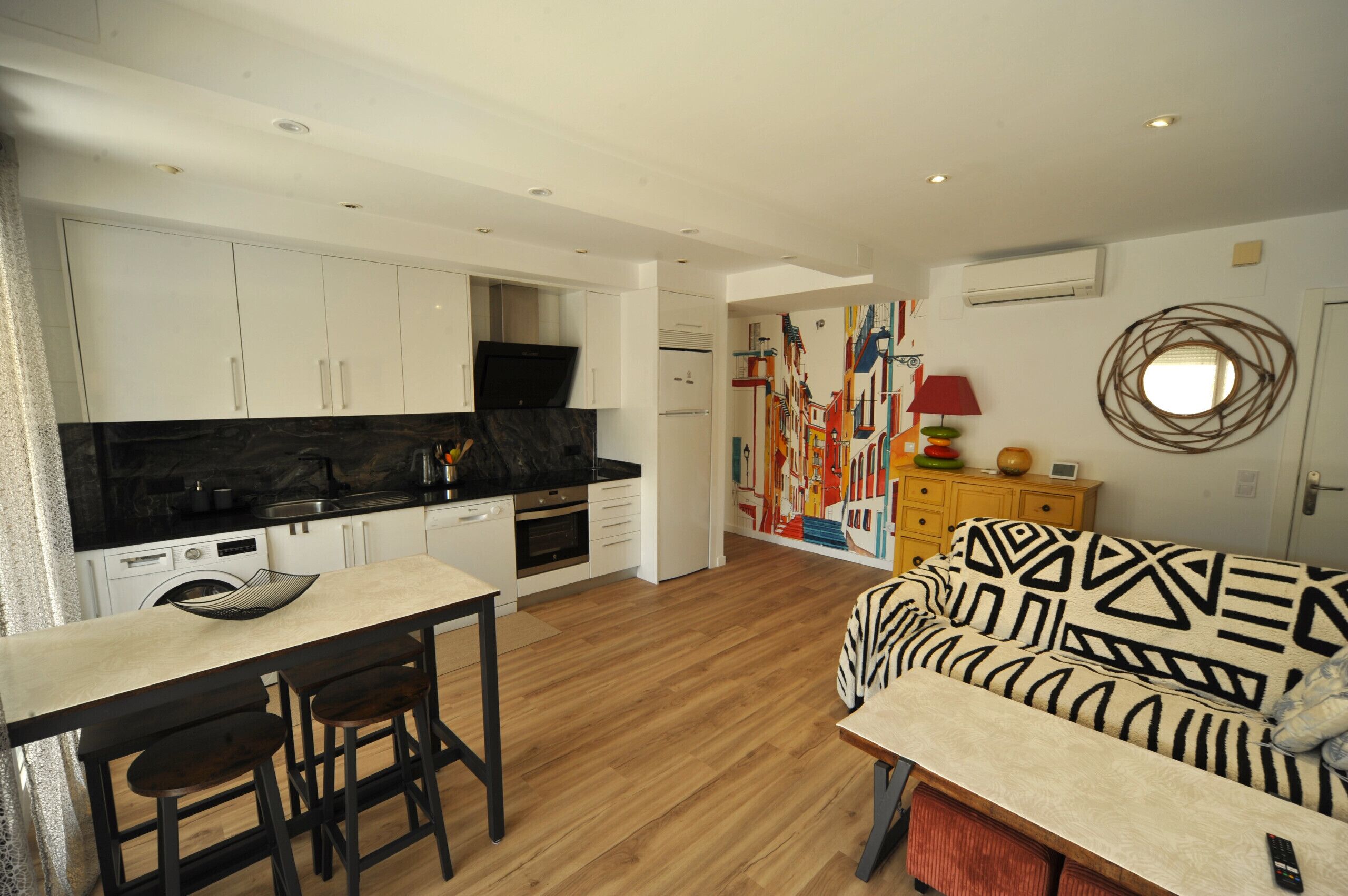 A modern kitchen with white cabinets, a black countertop, and a wooden dining table with bar stools.