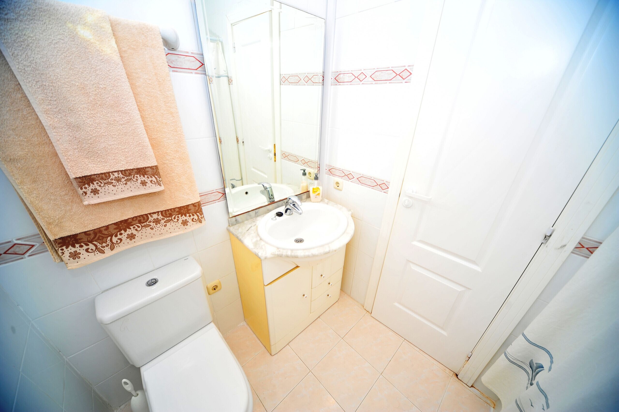 A bathroom with a toilet, sink, and mirror. There are towels hanging on the wall.