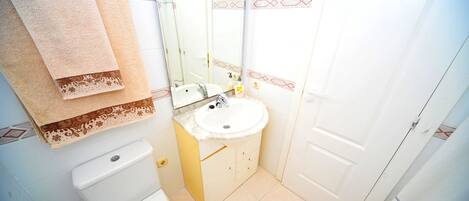 A bathroom with a toilet, sink, and mirror. There are towels hanging on the wall.